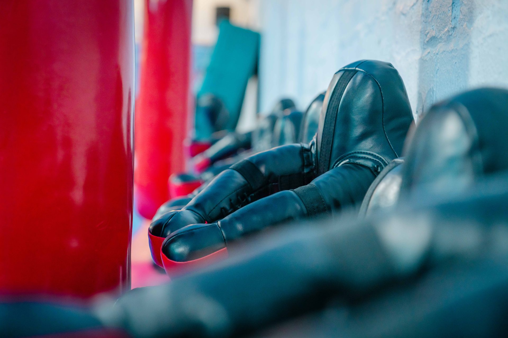 Detailaufnahme aufgereihter Boxhandschuhe neben den roten Sandsäcken der Trainingshalle.