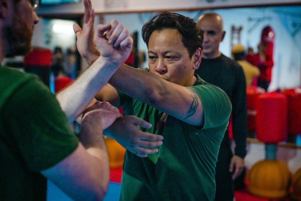 Wing Chun partner drill with a defensive movement between two trainees in the hall.