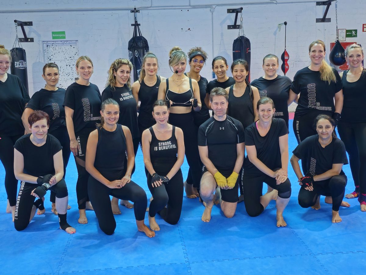 Die BODYCOMBAT-Gruppe stellt sich nach dem Kurs vor der Wand mit den Boxsäcken zum Teamfoto auf.