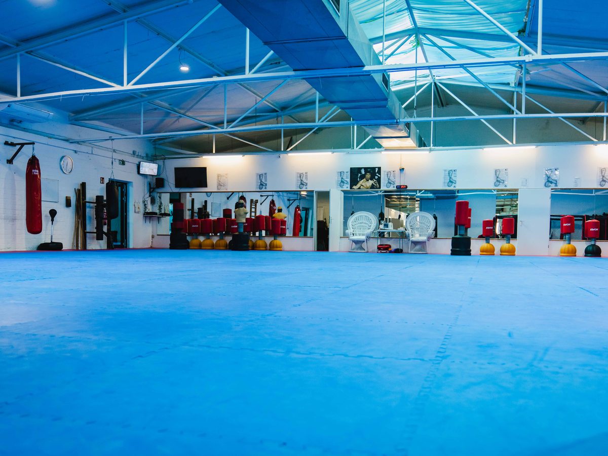 Weitwinkelaufnahme der Halle mit Boxring und roten Sandsäcken entlang der Wand.