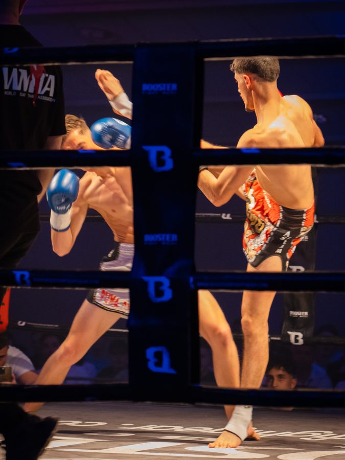 Zwei Kämpfer im Ring beim Schlagabtausch, einer deckt mit blauen Handschuhen ab.