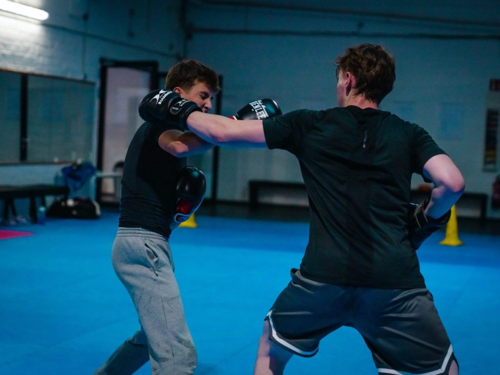 Zwei junge Männer im dynamischen Sparring mit Boxhandschuhen in der Trainingshalle.