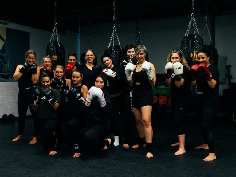 Elf Teilnehmerinnen mit Boxhandschuhen stehen in Kampfstellung vor den hängenden Boxsäcken.