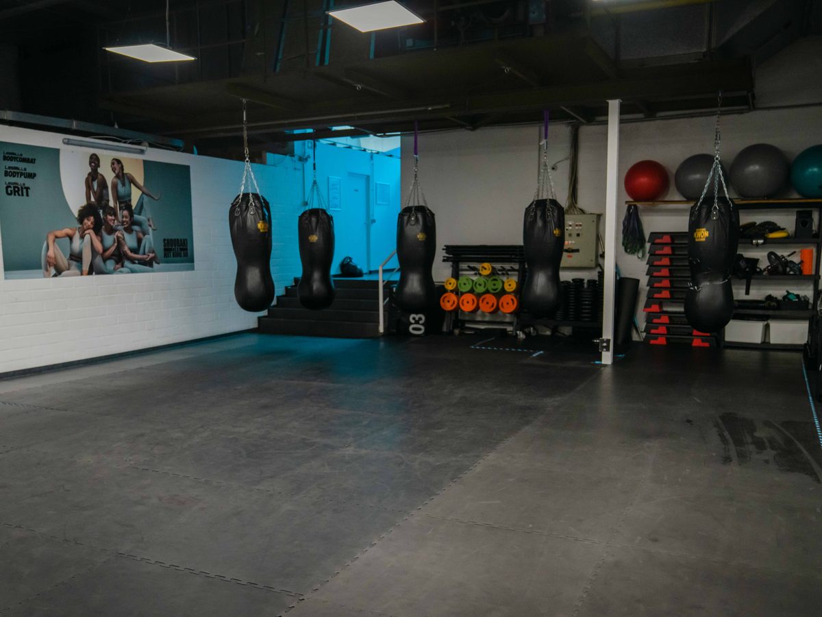Fitnessecke mit hängenden Sandsäcken, Medizinbällen und TRX-Bändern vor einem Wandposter.