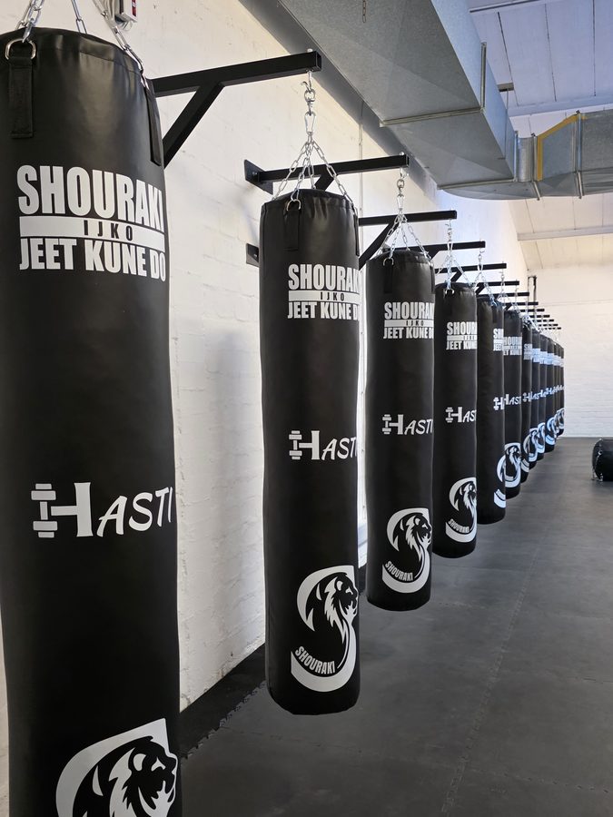 Reihe schwarzer Sandsäcke mit Shouraki-Jeet-Kune-Do-Branding, von der Hallendecke hängend.
