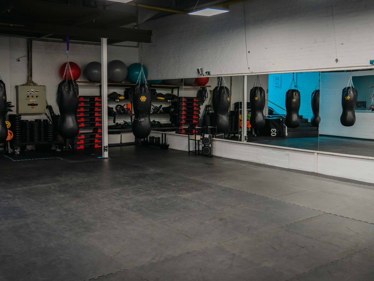 Kursraum mit Spiegelwand, Sandsäcken, Medizinbällen und dunklem Bodenbelag.