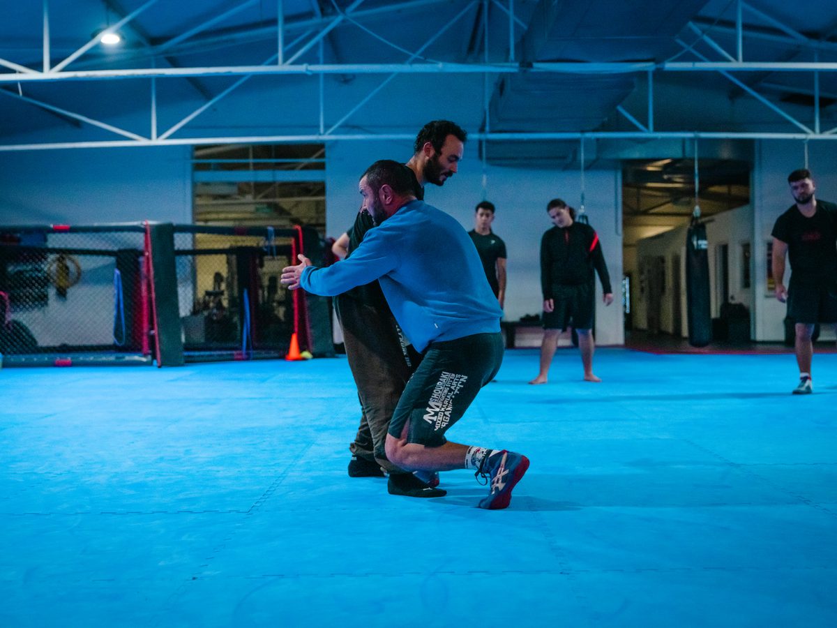 Grappling-Takedown: Ein Trainierender greift das Bein seines Partners und bringt ihn kontrolliert zu Boden.