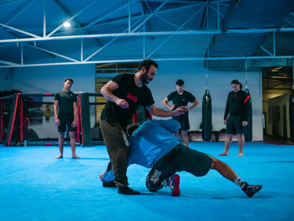 MMA oder Grappling: Was ist der Unterschied zu BJJ? 1 Trainierender bringt seinen Partner kontrolliert zu Boden, der Trainer beobachtet die Ausführung.