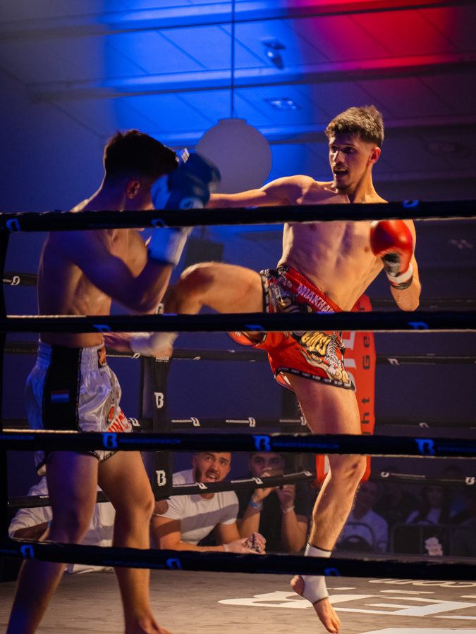 Kickboxen in Aachen 9 Kniestoß in der Luft, der Gegner geht in Deckung, kräftiges rot-blaues Ringlicht.
