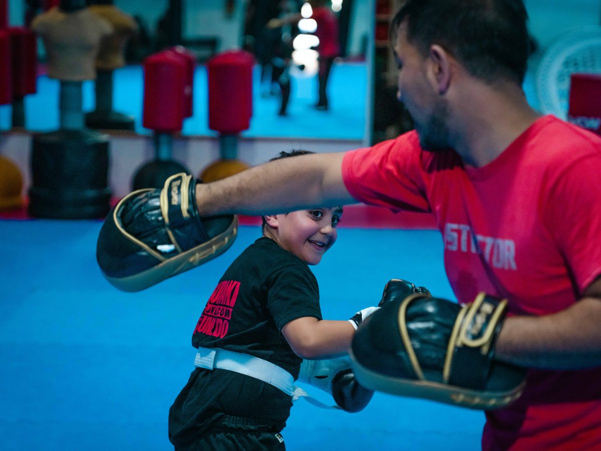 Nahaufnahme eines lachenden Jungen beim Pratzentraining, Arm und Pratze des Trainers im Vordergrund.