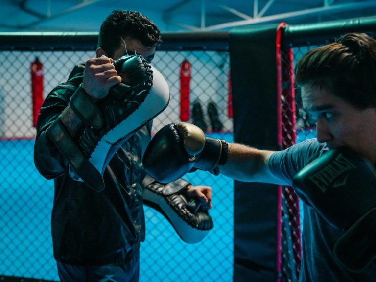 Nahaufnahme eines Schlagkombinations-Trainings mit Pratzen im MMA-Käfig.