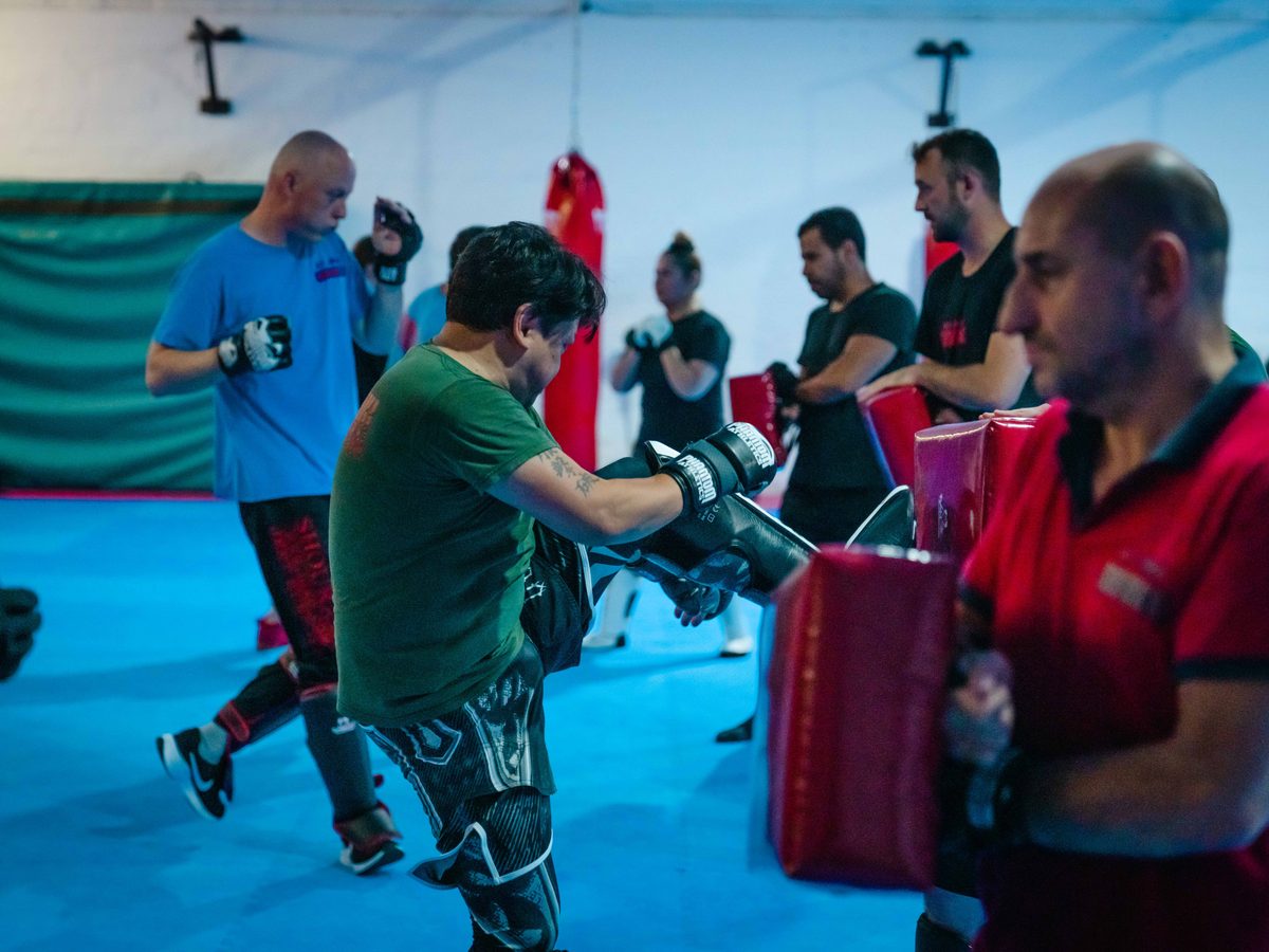 Schüler im grünen Shirt schlägt gegen die Pratzen, im Hintergrund weitere Trainingspaare.