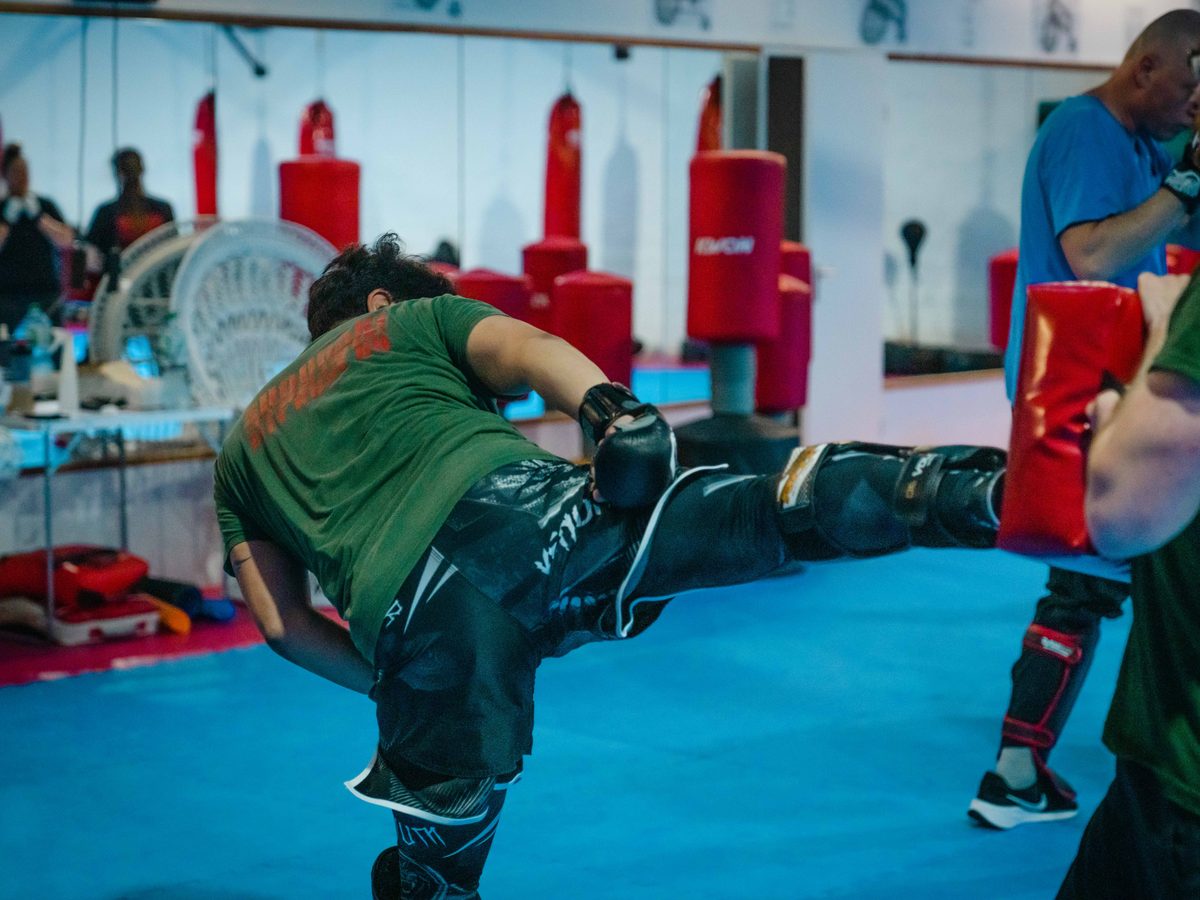 Dynamischer hoher Seitkick gegen ein Kickpad auf der blauen Trainingsmatte.