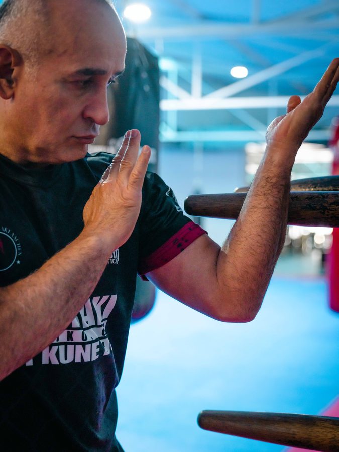 Der Sifu blockt mit beiden Unterarmen den Arm der hölzernen Wing-Chun-Puppe ab.