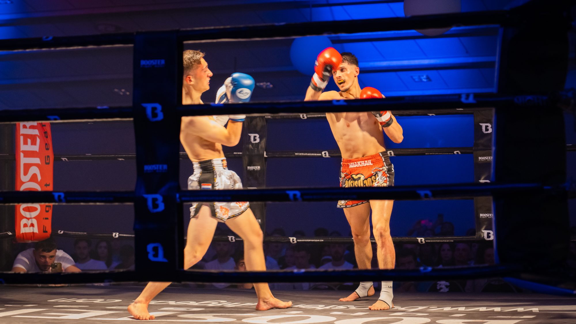 Zwei Kickboxer im Ring beim Schlagabtausch unter blauem Hallenlicht.