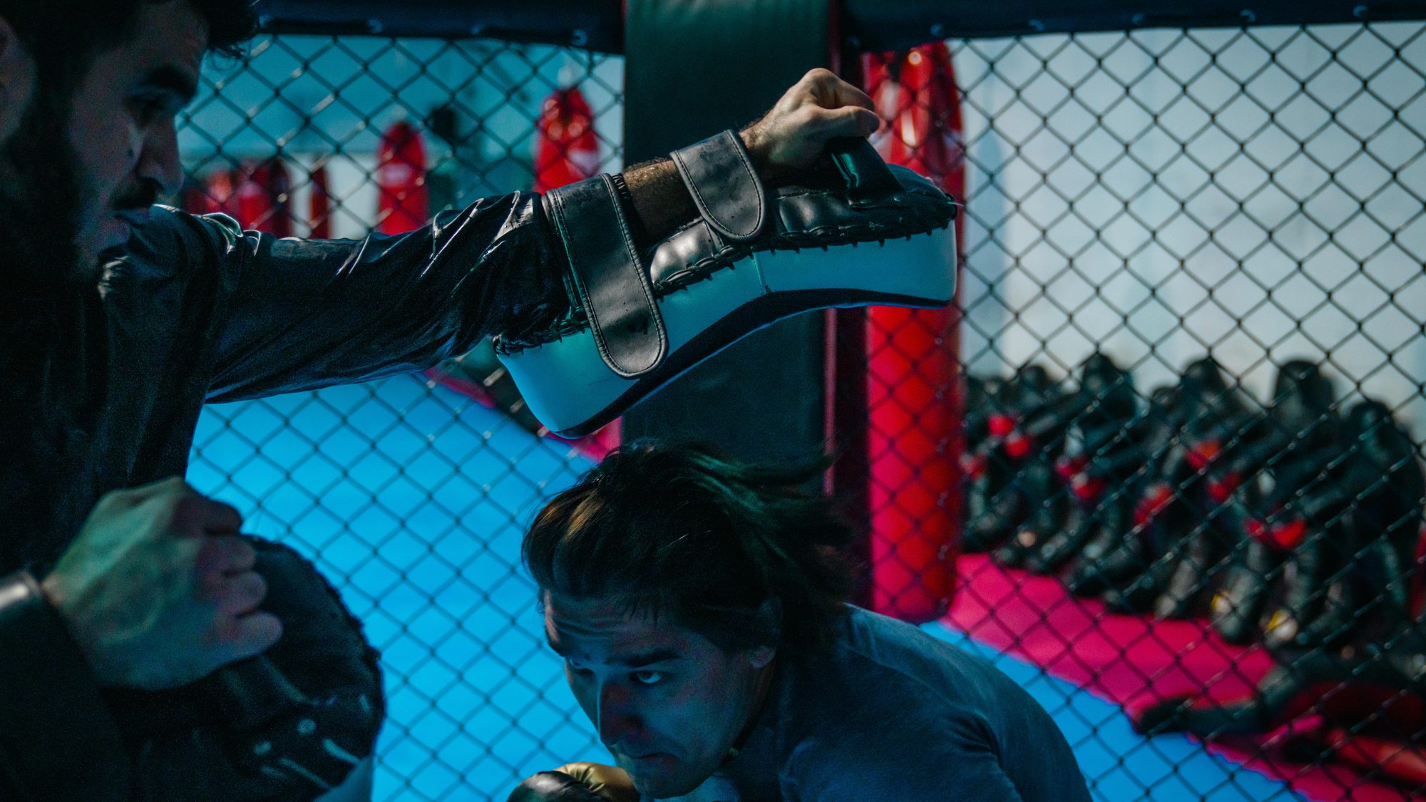 Kampfsport Aachen: Trainierender in Abwehrhaltung im MMA-Käfig, Handschuhe hängen an der Wand.