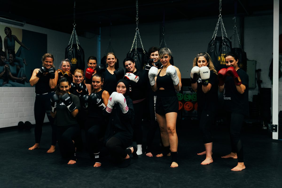 Die Teilnehmerinnen des Frauenkurses Fitness-Kickboxing und Thai-Boxing stehen mit Boxhandschuhen vor den hängenden Boxsäcken.