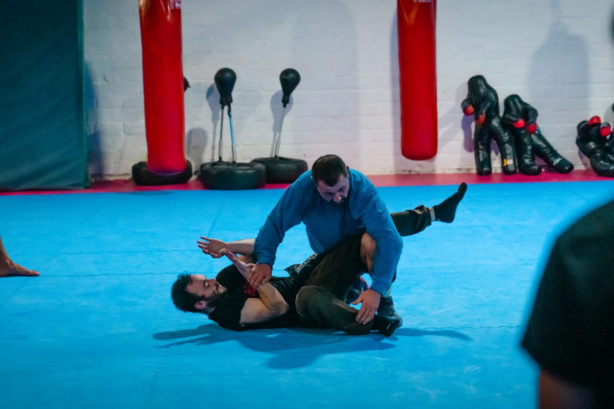 Im Bodenkampf hält ein Trainierender seinen Partner auf der Matte in kontrollierter Position.