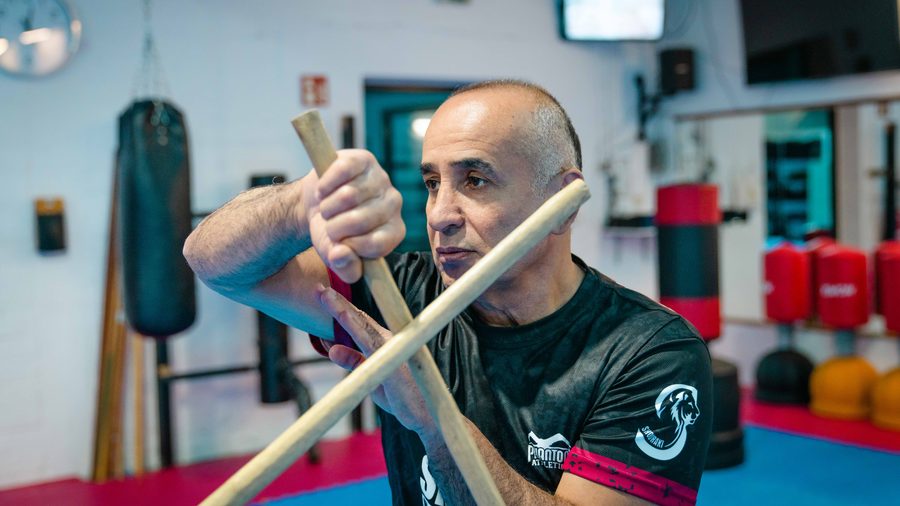 Kickboxen in Aachen 15 Der Sifu hält zwei Kali-Stöcke überkreuzt vor dem Gesicht und blickt konzentriert zur Seite.