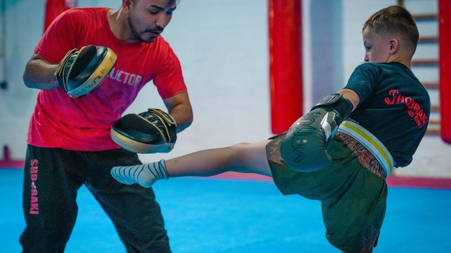 Kind trifft im Kindertraining mit einem Frontkick die Pratze des Trainers vor der Sprossenwand.