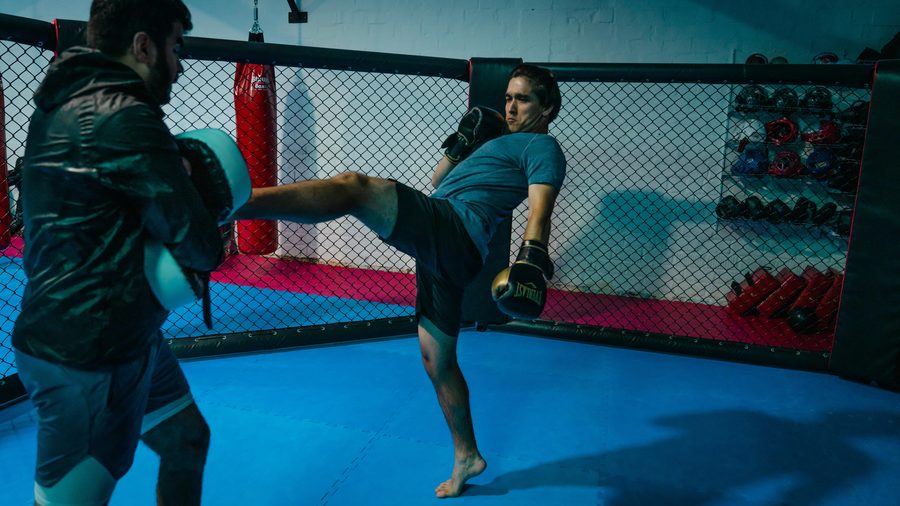 Kickboxen in Aachen 13 Im MMA-Käfig führt ein Trainierender einen hohen Roundhouse-Kick gegen die Pratze seines Partners aus.
