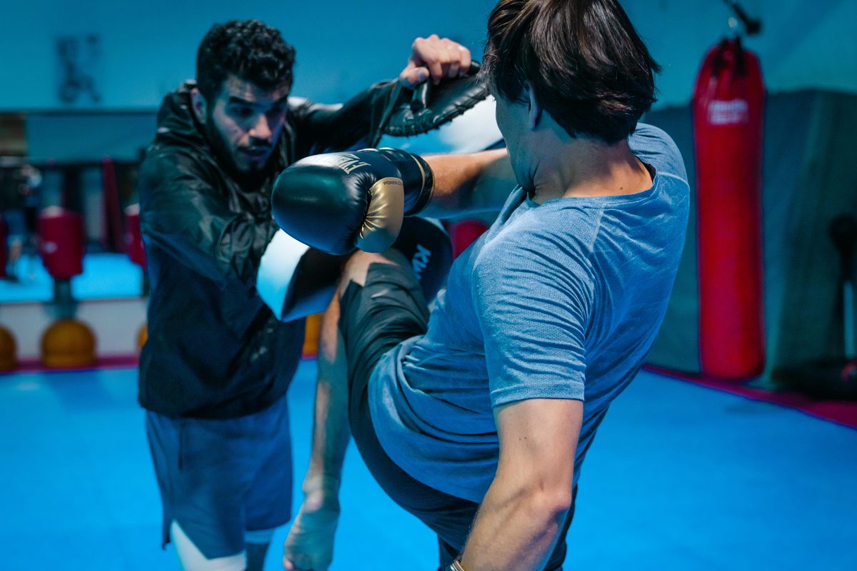 Ein Trainierender setzt im MMA-Training einen hohen Kick, den sein Partner mit dem Schlagpolster abfaengt.