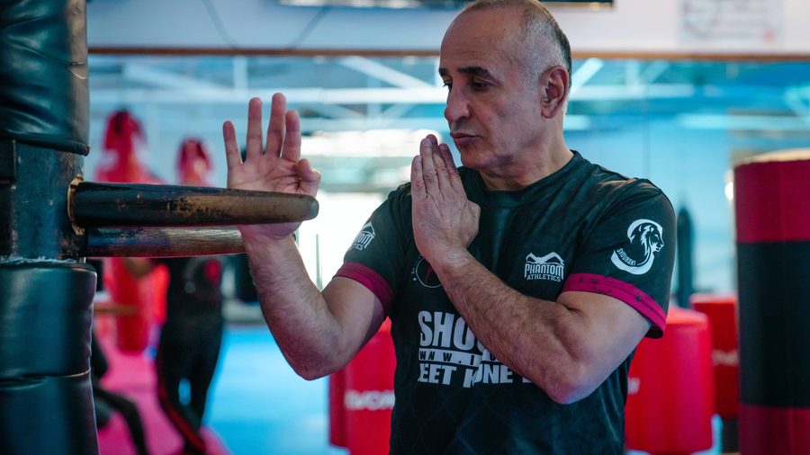 Der Sifu steht konzentriert in Grußhaltung vor der hölzernen Wing-Chun-Trainingspuppe.