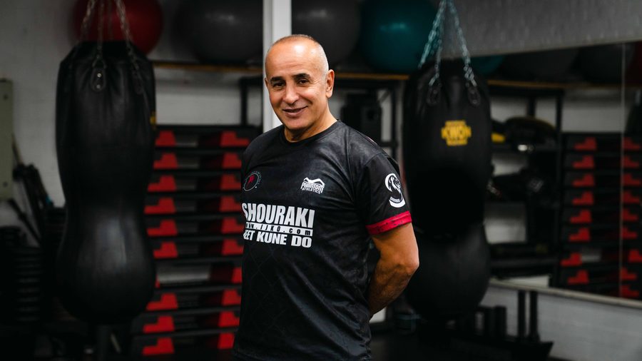 Dai Sifu Reza Shouraki steht vor den Sandsäcken der Halle, der Shouraki-Jeet-Kune-Do-Schriftzug ist auf dem Shirt zu lesen.