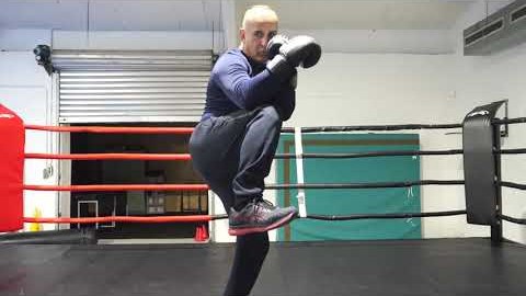 Beeld uit de lesvideo: de trainer tilt in de boksring met bokshandschoenen zijn knie op.