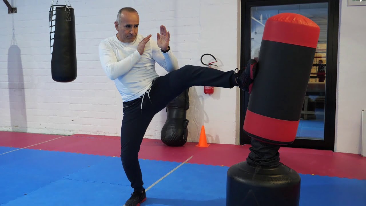 Beeld uit de lesvideo: de trainer trapt met geheven handen zijwaarts tegen een standzak.